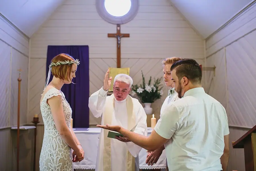 Bride and groom standing beside an officiant who looks down at a book.
