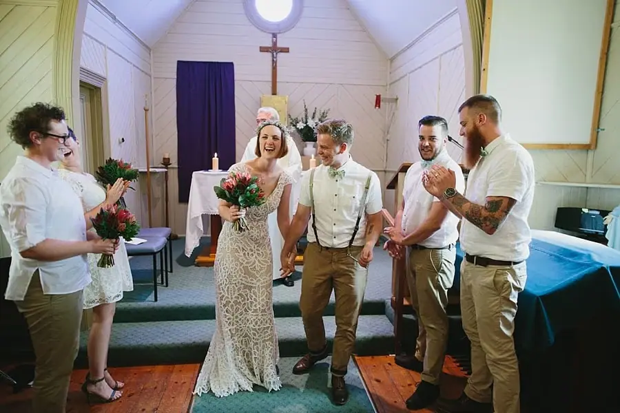 Bride and groom holding hands as their wedding party applauds.