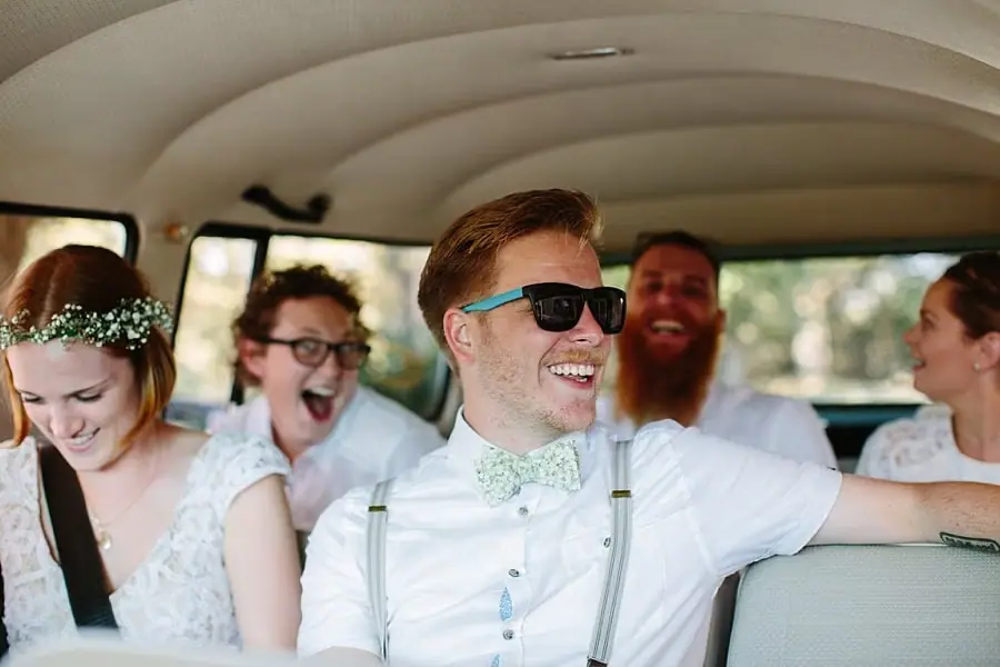 Bride and groom smiling with companions inside a van.