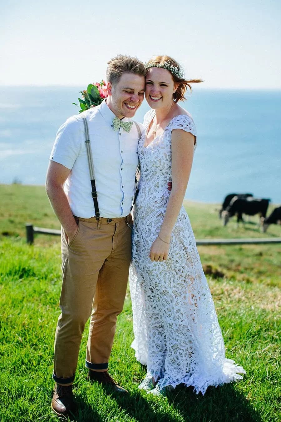 Bride and groom standing together on grass overlooking the sea.