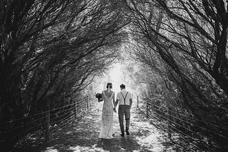 Black-and-white photograph of the couple walking beneath arching trees.