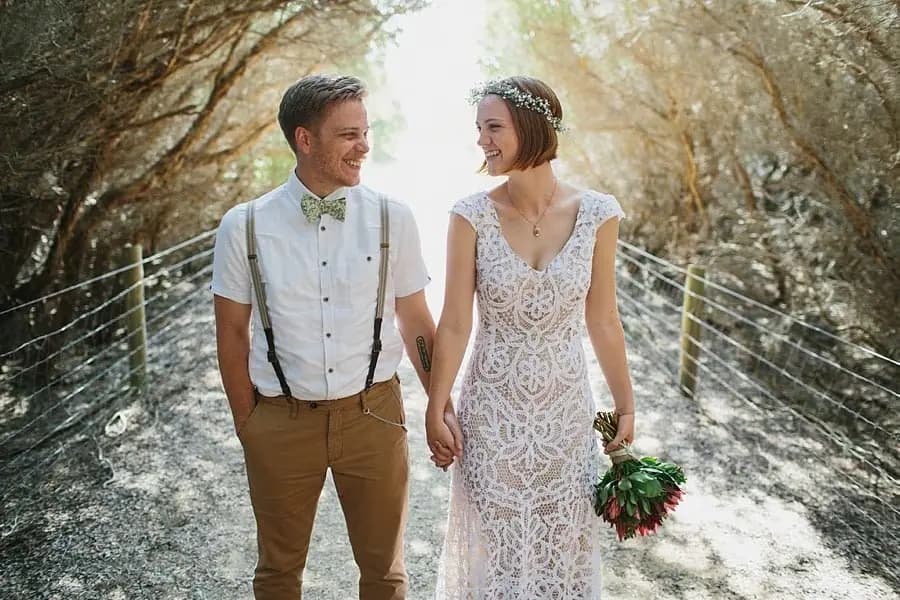 Bride and groom smiling at each other on a tree-lined path.