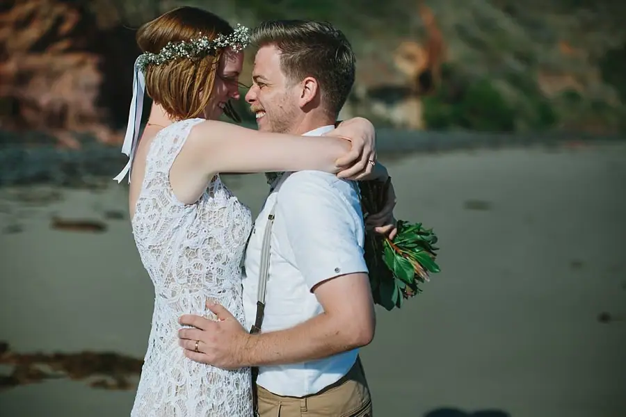 Bride and groom embracing beside the beach.