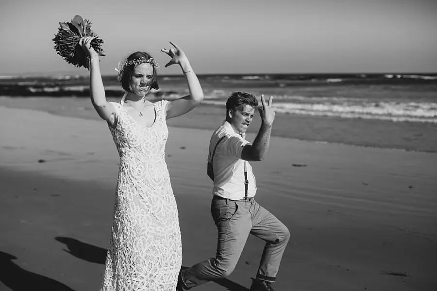 Black-and-white photograph of the couple raising their arms playfully on the beach.
