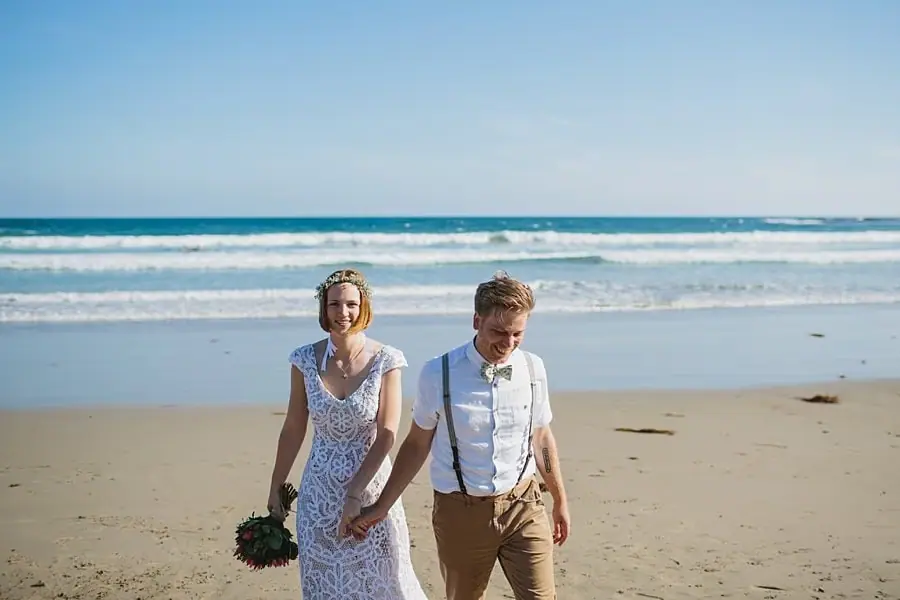 Bride and groom walking hand in hand across the sand.