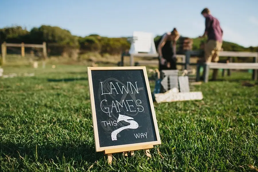 Chalkboard directing guests toward lawn games on a grassy field.