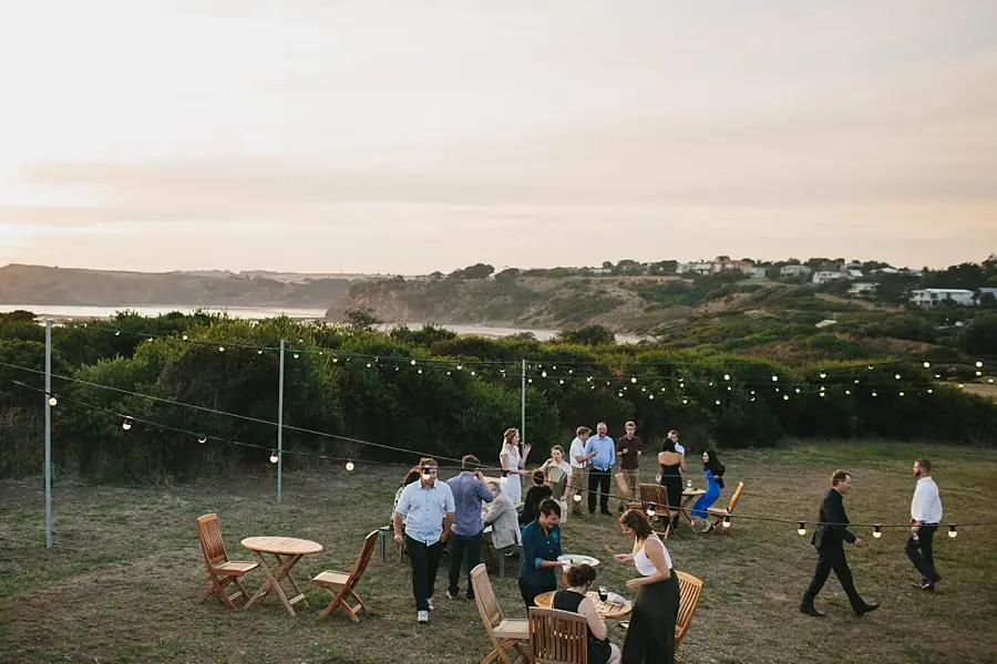 Wedding guests mingling on a grassy lawn in warm evening light.