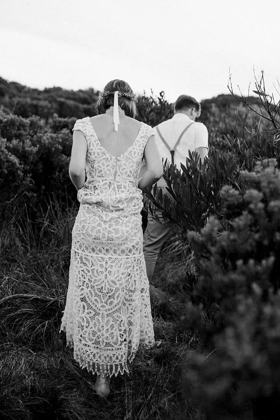 Black-and-white photograph of the couple walking through coastal shrubs.