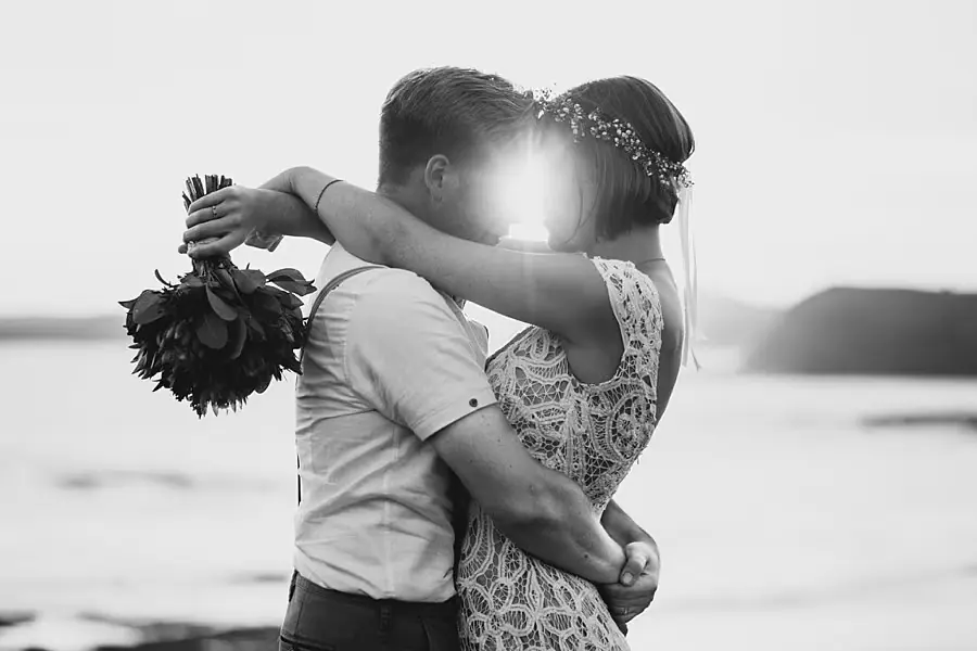 Black-and-white photograph of the couple embracing with sunlight behind them.