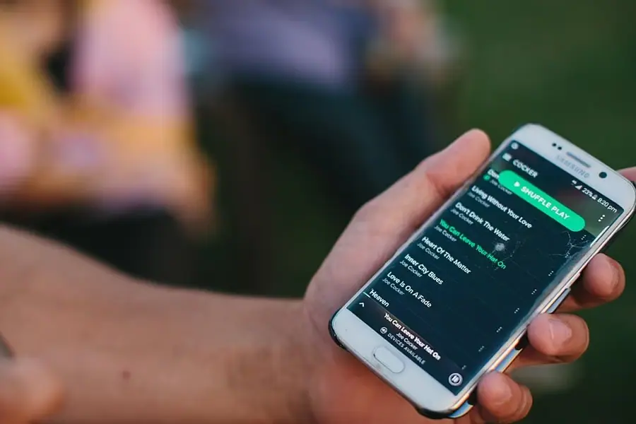 Close-up of a hand holding a phone displaying a music playlist.