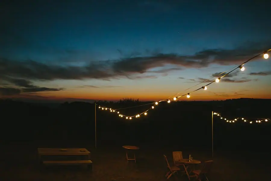 Strings of lights glowing over an outdoor reception area at dusk.