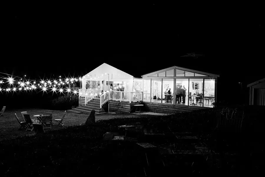 Black-and-white view of the illuminated reception house and marquee at night.