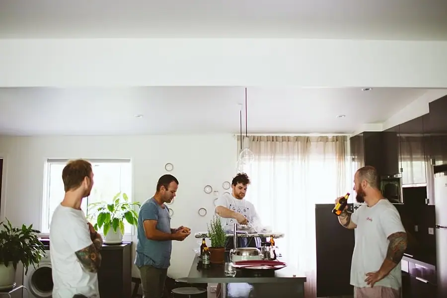 Men chat and prepare drinks around a kitchen island.