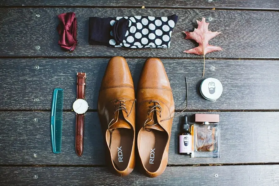 Wedding shoes, watch, bow tie and accessories arranged on wooden boards.