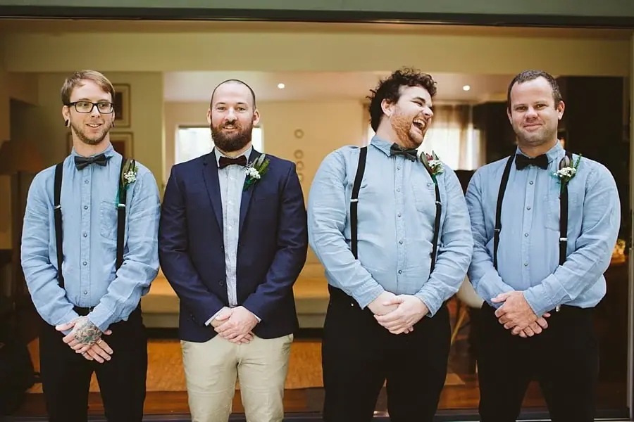 Groom and groomsmen laugh together in front of a doorway.