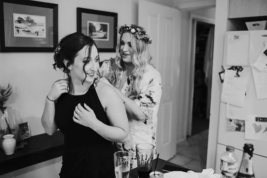 Black and white photograph of a woman helping a friend with her dress.