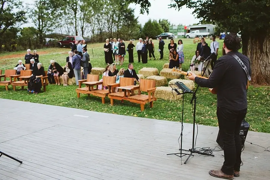 Musician performs on a deck before guests gathering at garden benches.
