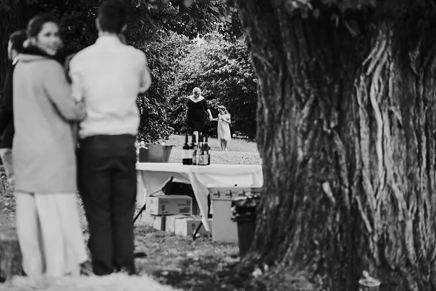 Black and white view past a tree toward the couple approaching the ceremony.