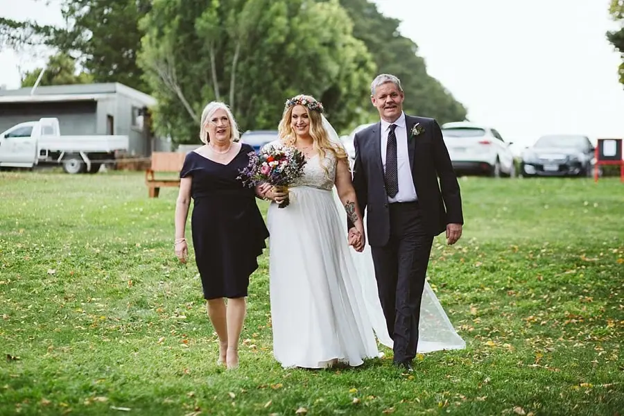 Bride approaches across the lawn between two guests.