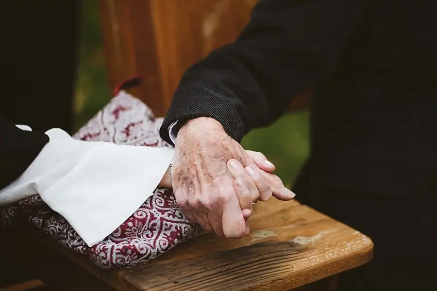 Close view of an older guest's hand beside tissues on a wooden bench.