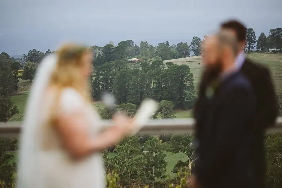 Soft-focused view of the bride reading her vows with green hills beyond.