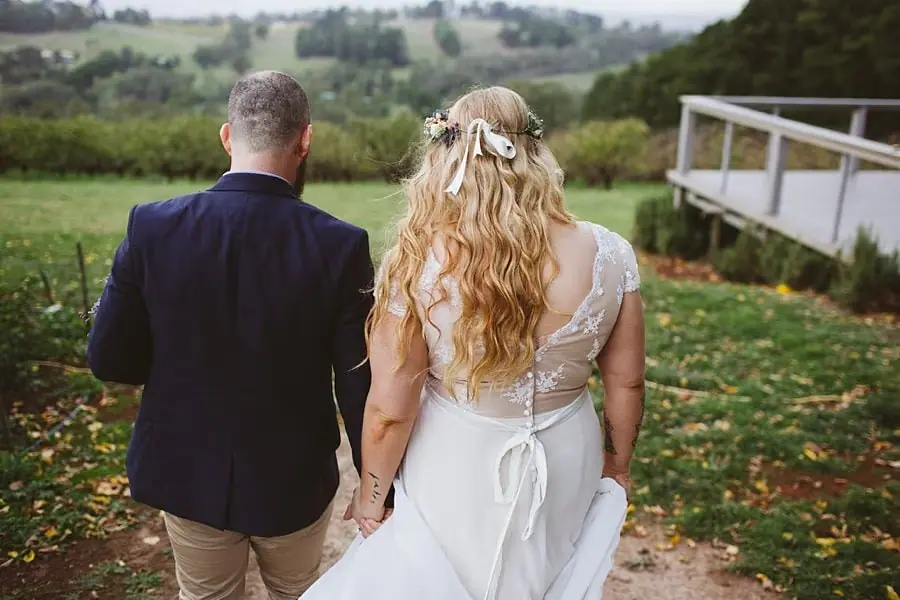 Bride and groom walking hand in hand down a garden path overlooking the hills.