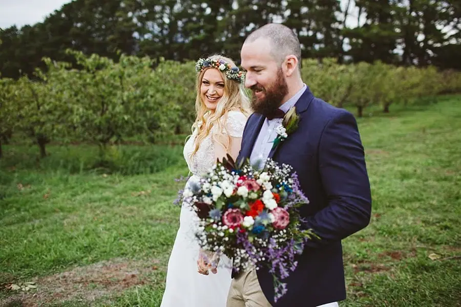 Groom carrying a colourful bouquet while walking beside the bride outdoors.