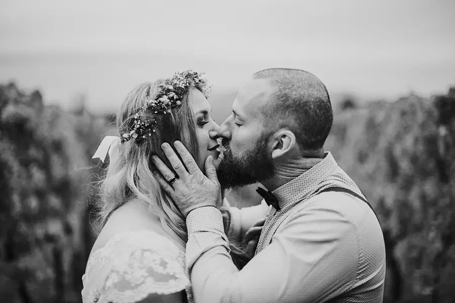 Black-and-white close-up of the bride and groom kissing in the vineyard.