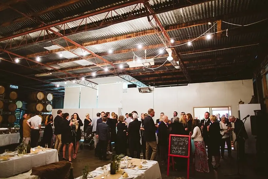 Guests gathering inside a reception space beneath strings of lights.