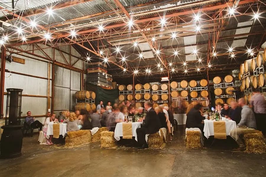 Wide view of guests seated beneath festoon lights in a barrel-lined reception room.