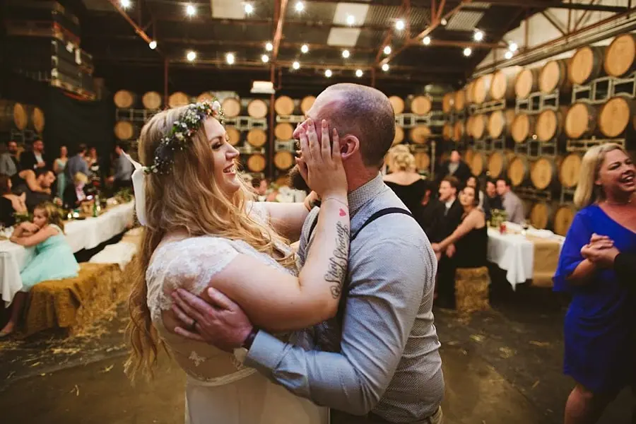 Bride touching the groom's face as they dance beneath festoon lights.