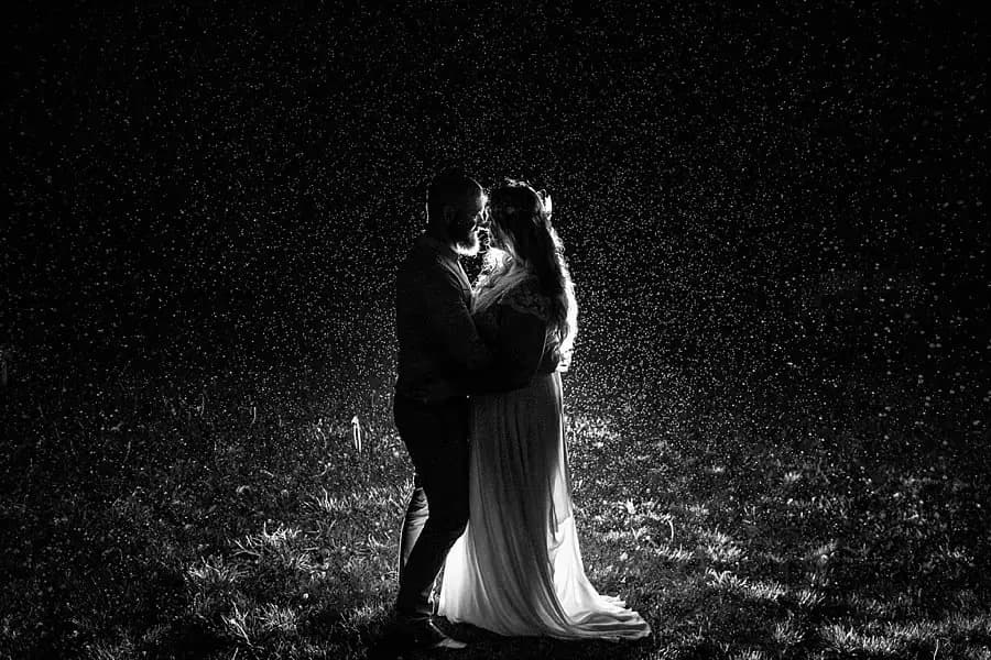 Black-and-white portrait of the bride and groom kissing outside at night.