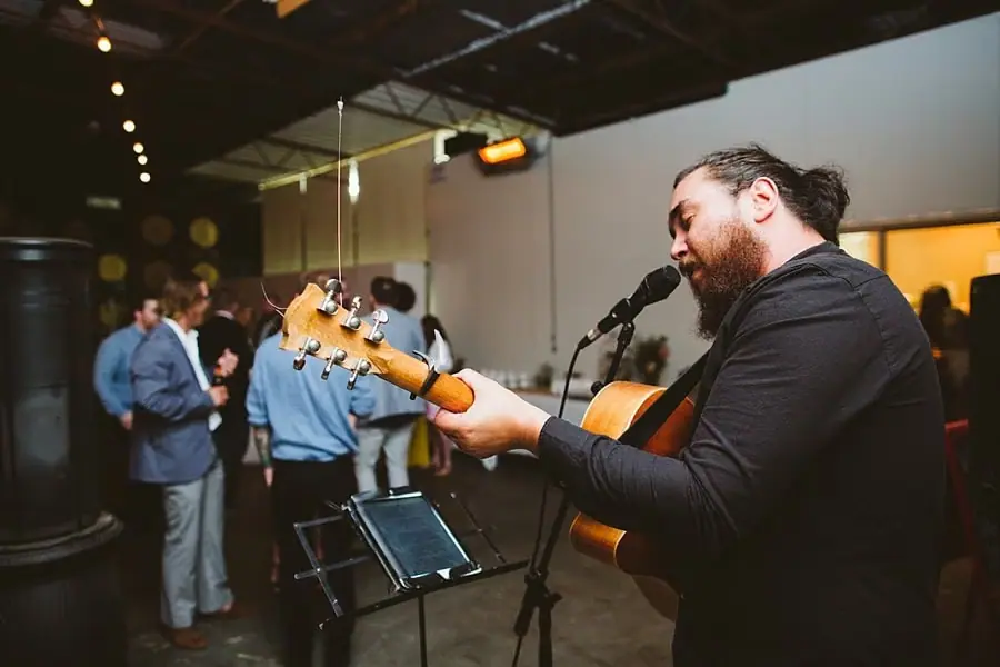 Guitarist singing into a microphone while guests dance behind him.
