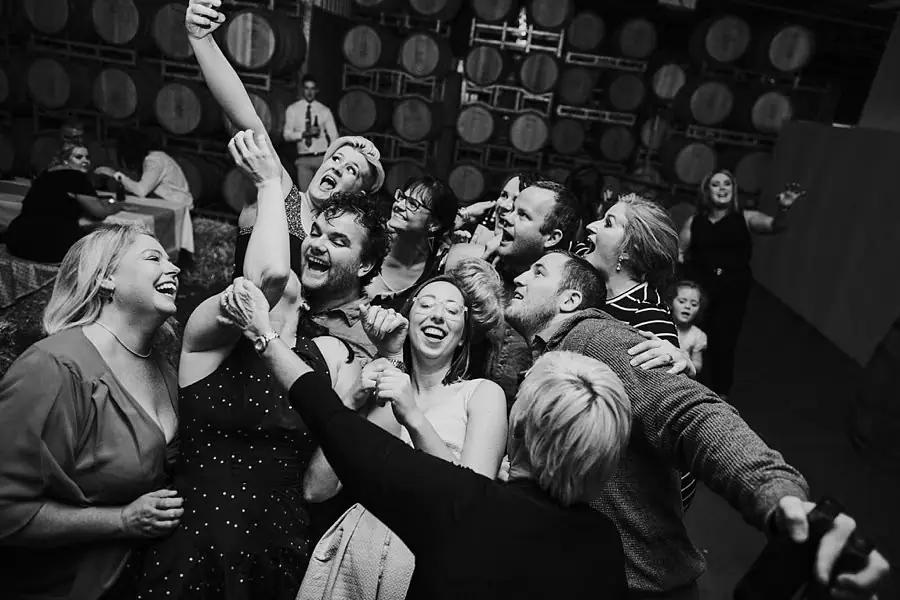 Black-and-white photograph of laughing guests crowding together on the dance floor.