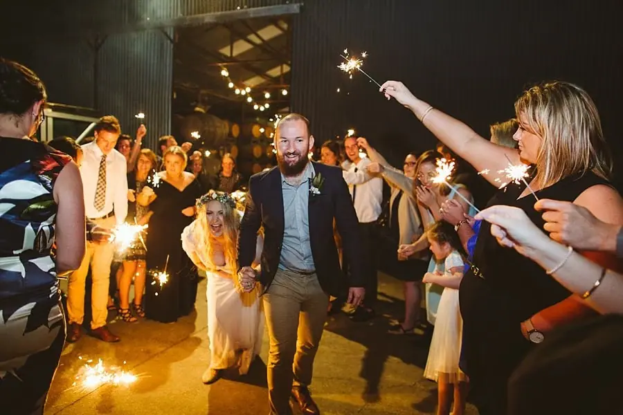 Bride and groom walking through guests holding sparklers outside at night.