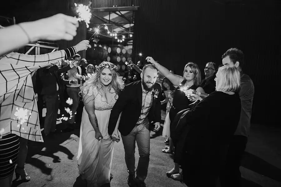 Black-and-white photograph of the couple passing beneath guests' sparklers.