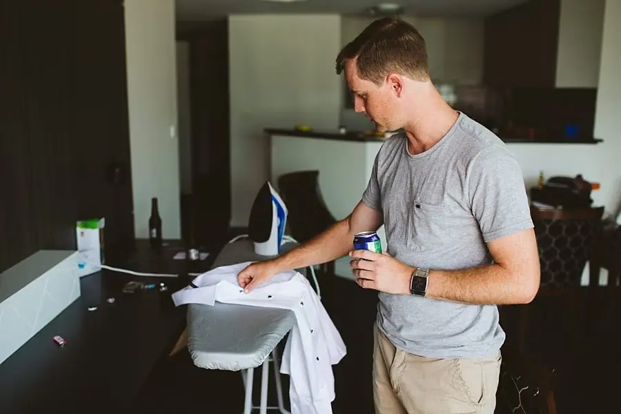 Man holding a drink beside a white shirt laid on an ironing board.