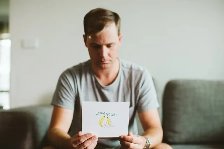 Man seated on a sofa reading a card.