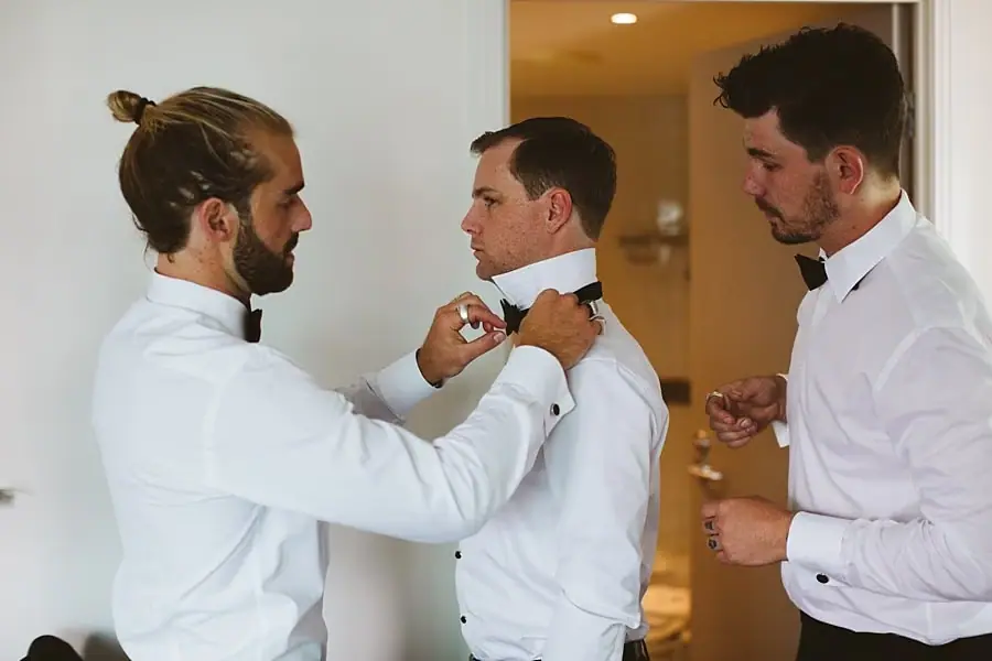 Man helping another man fasten his bow tie.