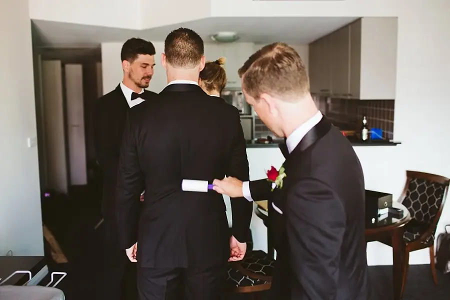 Men in dark suits checking their clothing in a kitchen.