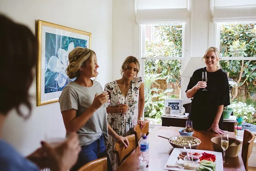 Women holding drinks around a table in a bright room.