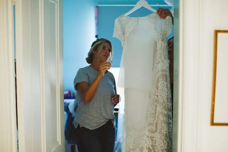 Woman holding up a white lace wedding dress in a doorway.
