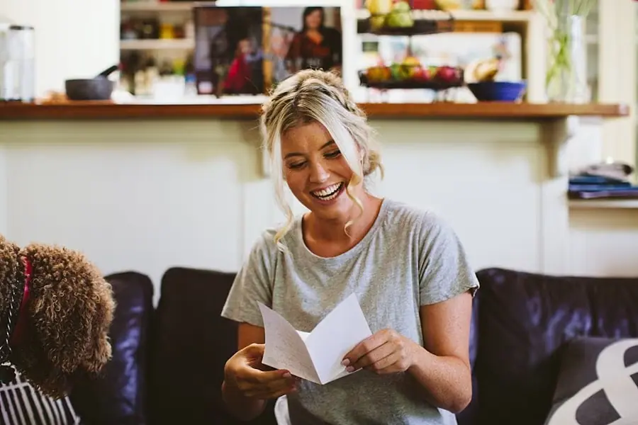 Woman smiling while reading a folded note on a sofa.