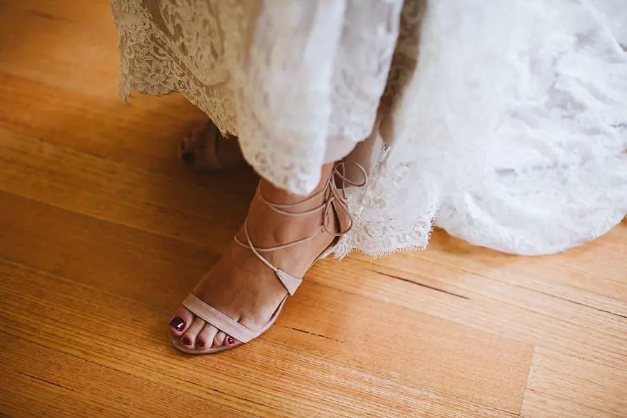Close-up of a pink heeled sandal beneath a lace wedding dress.