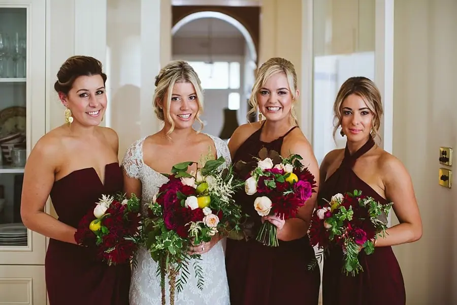 Bride and three women in burgundy dresses holding colorful bouquets.