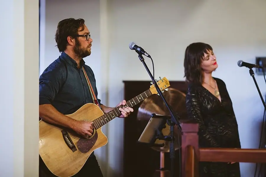 Guitarist and singer performing beside microphones indoors.