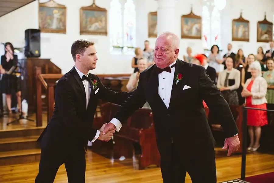 Groom greeting a suited man beside the church aisle.