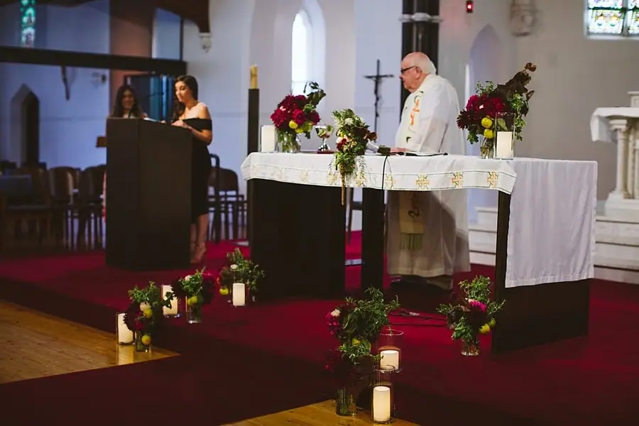 Wedding ceremony taking place beside a flower-decorated church altar.