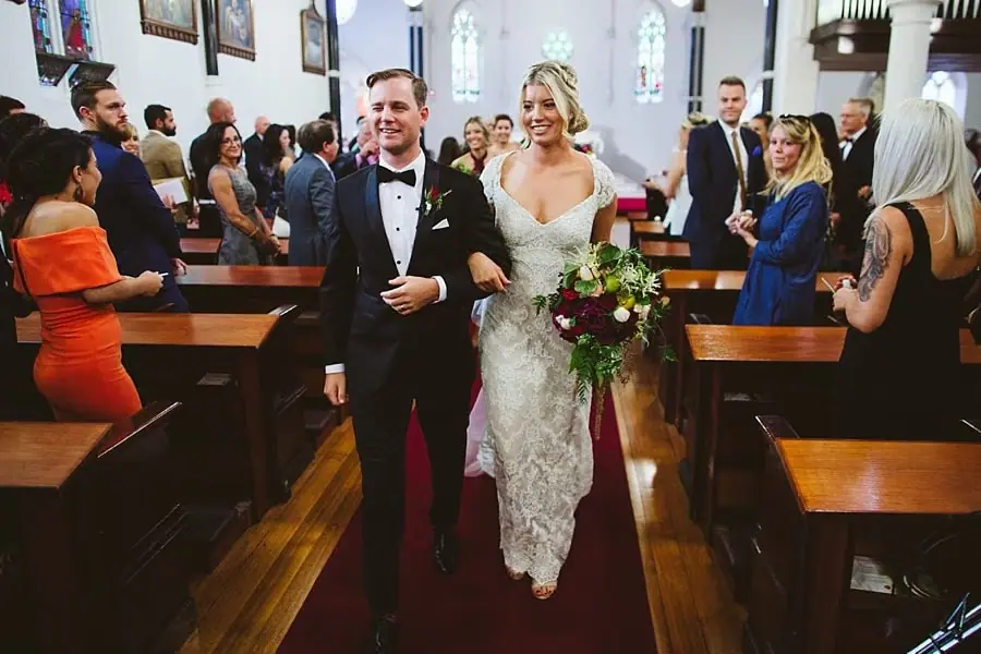 Bride and groom smiling as they walk down the church aisle.