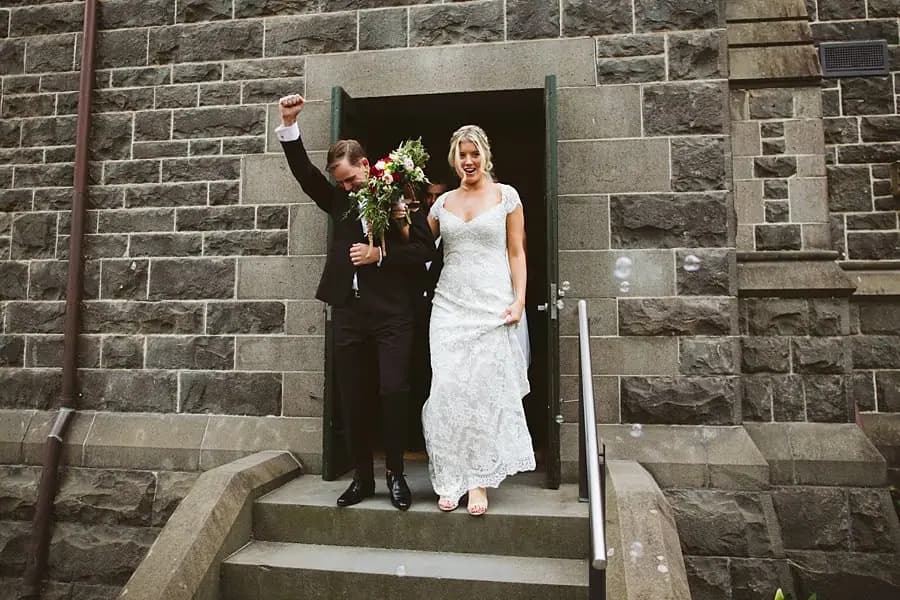 Bride and groom standing on stone church steps as the groom raises his arm.